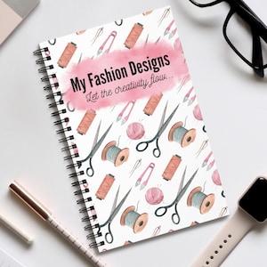 Può includere: Un quaderno a spirale bianco con un design ad acquerello rosa. Il quaderno ha uno sfondo ad acquerello rosa con un motivo di forbici, rocchetti di filo e spilli. Il testo "My Fashion Designs Let the creativity flow..." è stampato in nero sulla copertina.