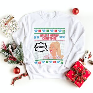 May include: White Christmas sweater with a cartoon image of a woman with blonde hair and a red and white polka dot dress. The sweater has a green and white snowflake pattern and the text "Have a Merry Christmas" and "Or What?!".