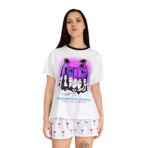 May include: White pajama set with a graphic print of a building with palm trees and five women. The text "Vanderpump Legends West Hollywood" is printed on the shirt. The pajama shorts have a purple martini glass pattern.