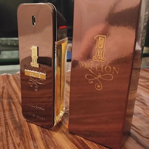 Op de afbeelding: Een Paco Rabanne 1 Million Privé parfumfles en de bijbehorende rechthoekige doos. Beide items hebben een metallic bruine afwerking met goudkleurige letters 1 Million Privé. De fles heeft een zijkant van helder glas met amberkleurige vloeistof.