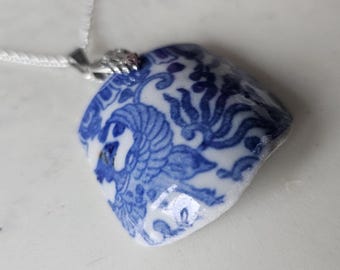 May include: A blue and white porcelain pendant necklace with a floral design. The pendant is shaped like a small bowl and has a silver chain.