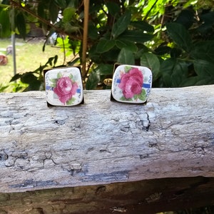 May include: A pair of square cufflinks with a gold metal frame and a white porcelain centre featuring a pink rose with blue and white accents.