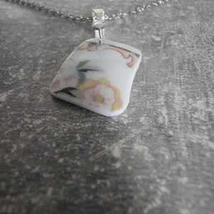 May include: A silver chain necklace with a white porcelain pendant featuring a floral design in pink, yellow, and green.
