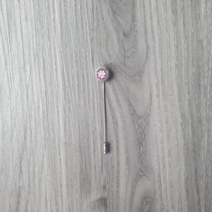 May include: A silver pin with a white and pink flower design on the top.