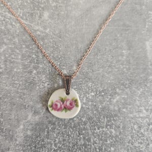 May include: A delicate rose-patterned porcelain pendant necklace with a rose gold chain.