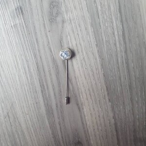 May include: A silver pin with a white ceramic top featuring a blue floral design.