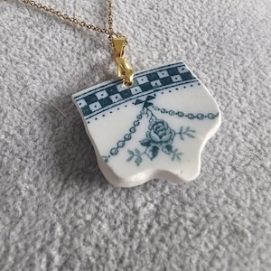 Puede incluir: Un collar de cadena dorada con un colgante hecho de una pieza de porcelana vintage con un diseño floral azul y blanco.