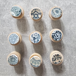 May include: Nine round wooden knobs with blue and white floral patterns. The knobs are arranged in a grid pattern on a gray surface.