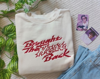 May include: A cream-colored sweatshirt with red embroidered text that reads "Brought The Reggae Back".