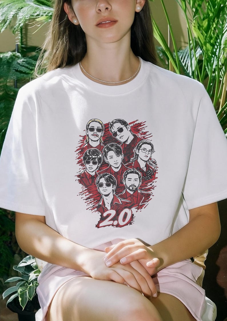 May include: White t-shirt featuring a graphic of seven people with sunglasses and the number "2.0" in red. The design is set against a red splatter background. The shirt is a casual wear item.