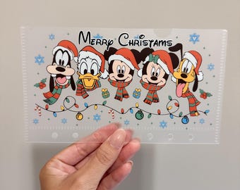 Könnte beinhalten: Eine durchscheinende Kunststoff-Einlage mit einer bunten Grafik von fünf Zeichentrickfiguren, die rote Weihnachtsmützen und gestreifte Schals tragen. Der Text Merry Christams steht über den Figuren, ergänzt durch blaue Schneeflocken und eine bunte Lichterkette.