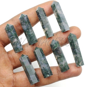 Peut inclure: Huit pointes de cristal en agate mousse, chacune avec un motif unique d'inclusions vertes et blanches. Les formes hexagonales polies sont tenues dans une main sur fond blanc. Ces obélisques en pierres précieuses mesurent environ 7.6 cm de haut.