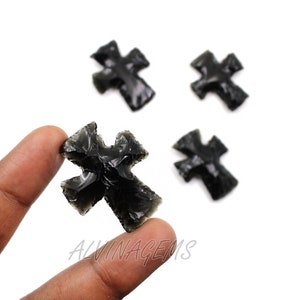 May include: Four black obsidian arrowheads shaped like crosses. One arrowhead is being held by a finger.