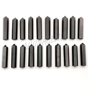 K&ouml;nnte beinhalten: Ein Set mit 18 schwarzen Obsidian-Kristallspitzen, jede etwa 5 cm lang. Die Spitzen sind in zwei Reihen zu je neun angeordnet, wobei die Spitzen nach oben zeigen.