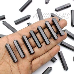 K&ouml;nnte beinhalten: Eine Hand h&auml;lt eine Sammlung schwarzer Obsidianspitzen. Die Spitzen sind glatt und poliert, mit einer scharfen Spitze. Die Spitzen sind f&auml;cherf&ouml;rmig angeordnet, wobei die Spitzen nach au&szlig;en zeigen.