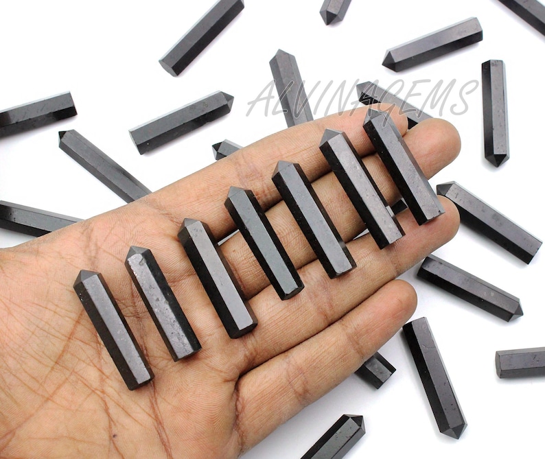 K&ouml;nnte beinhalten: Eine Hand h&auml;lt eine Sammlung schwarzer Obsidianspitzen. Die Spitzen sind glatt und poliert, mit einer scharfen Spitze. Die Spitzen sind f&auml;cherf&ouml;rmig angeordnet, wobei die Spitzen nach au&szlig;en zeigen.