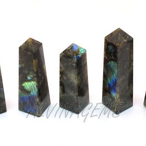 May include: Five polished labradorite crystal obelisks. The stones are dark gray with iridescent blue and green flashes. The obelisks are rectangular with a pointed top. The text "ALVINAGEMS" is visible on one of the obelisks.