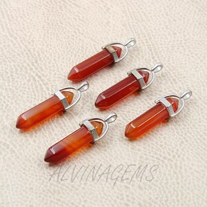 Peut inclure: Cinq pendentifs en pierres précieuses rouge-orange avec des boucles en métal argenté. Les pendentifs sont hexagonaux et pointus en bas. Le texte "ALVINAGEMS" est visible en bas de l'image.