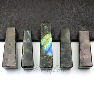 May include: Five polished labradorite obelisks. The obelisks are rectangular with a pointed top. The stones have a mix of gray, blue, and yellow colors. The text "ALVINTAGEEMS" is visible on the bottom.