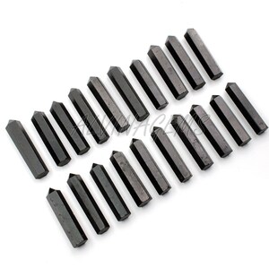K&ouml;nnte beinhalten: Zwanzig schwarze Obsidian-Kristallspitzen, die in Reihen auf einem wei&szlig;en Hintergrund angeordnet sind. Die Spitzen sind etwa 5 cm lang und haben eine glatte, polierte Oberfl&auml;che.