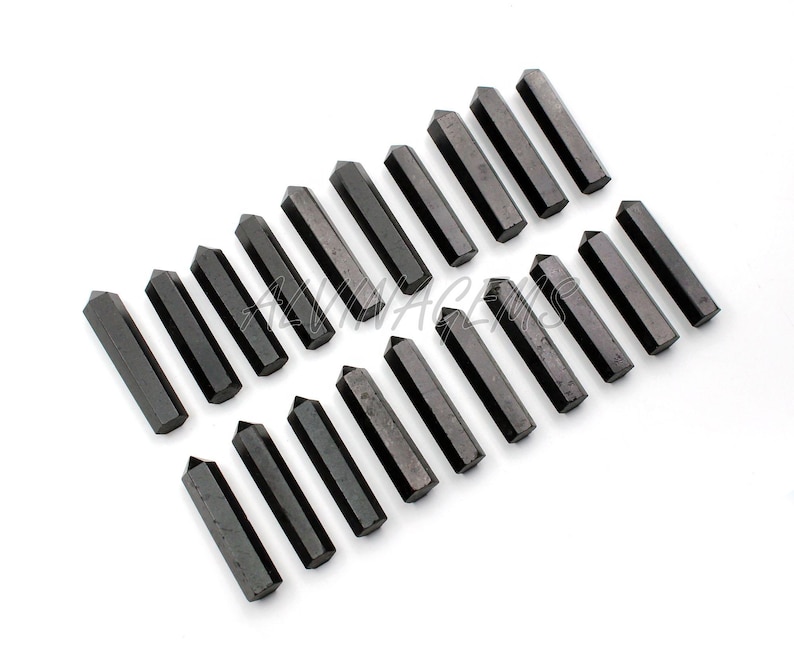 K&ouml;nnte beinhalten: Zwanzig schwarze Obsidian-Kristallspitzen, die in Reihen auf einem wei&szlig;en Hintergrund angeordnet sind. Die Spitzen sind etwa 5 cm lang und haben eine glatte, polierte Oberfl&auml;che.