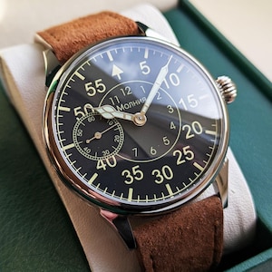 May include: A silver wristwatch with a black face and brown leather strap. The watch face has white markings and the word "Молния" printed on it.