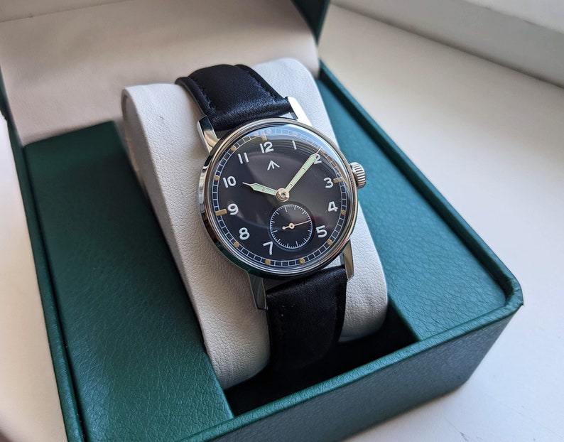 May include: A black leather wristwatch with a silver case and a black face. The watch has white numerals and a silver second hand.