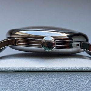 May include: A silver wristwatch with a round face and a black leather band. The watch has a silver crown on the right side of the case.
