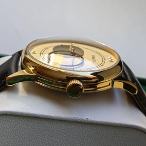 May include: A gold-tone wristwatch with a white face and black hands. The watch has a brown leather band and a round case.