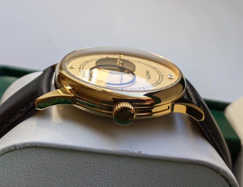 May include: A gold-tone wristwatch with a white face and black hands. The watch has a brown leather band and a round case.