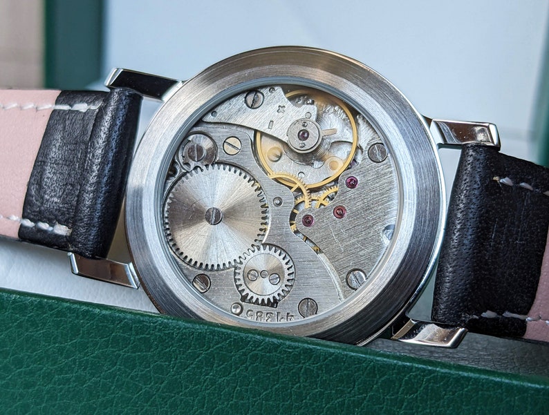 May include: A silver watch with a black leather band and a clear case back revealing the inner workings of the watch mechanism.
