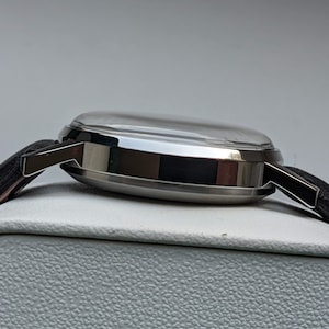 May include: A silver wristwatch with a black leather band. The watch has a round face and a silver case.
