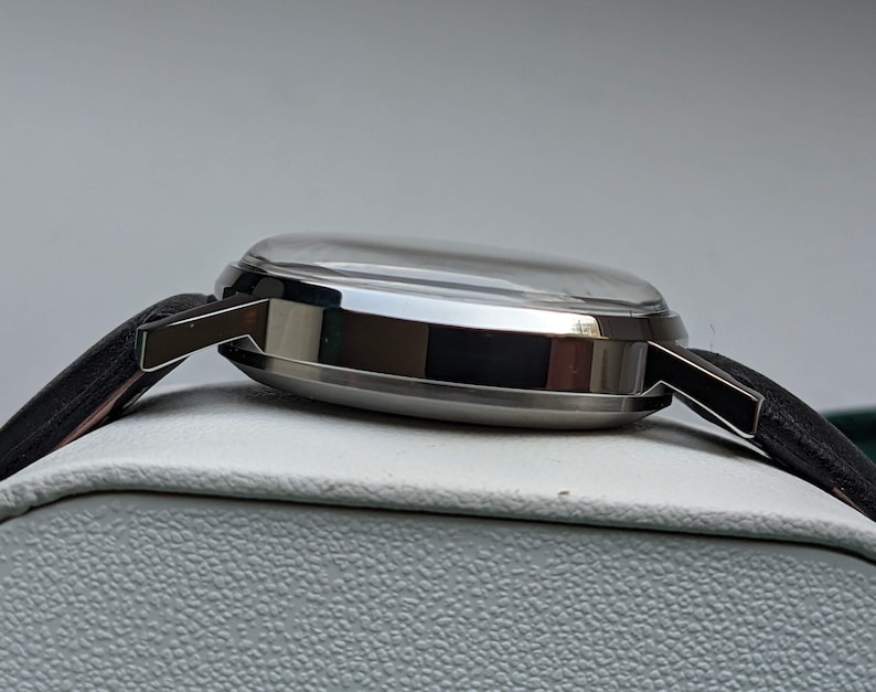 May include: A silver wristwatch with a black leather band. The watch has a round face and a silver case.