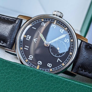 May include: A black and silver wristwatch with a black leather band. The watch face has white Arabic numerals and a small subdial at the 6 o'clock position.