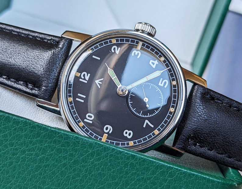 May include: A black and silver wristwatch with a black leather band. The watch face has white Arabic numerals and a small subdial at the 6 o'clock position.