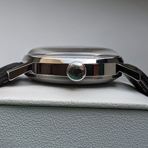 May include: A silver wristwatch with a black leather band. The watch has a round face and a silver case. The watch is on a white surface.