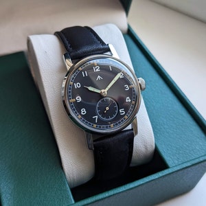 May include: A black leather wristwatch with a silver case and a black face. The watch has white numerals and a gold second hand.