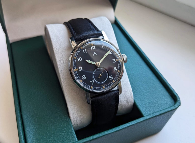 May include: A black leather wristwatch with a silver case and a black face. The watch has white numerals and a gold second hand.