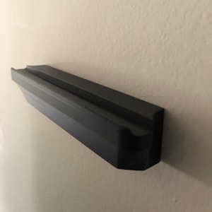 Puede incluir: Un estante de pared de plástico negro con una superficie texturizada.