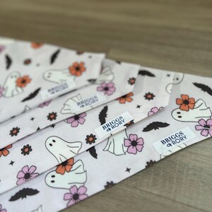 K&ouml;nnte beinhalten: Vier wei&szlig;e Stoff-Hundehalst&uuml;cher mit einem Geister- und Blumenmuster. Die Halst&uuml;cher haben ein schwarz-wei&szlig;es Etikett mit der Aufschrift "Briggs + Rory".
