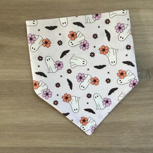 K&ouml;nnte beinhalten: Wei&szlig;es Bandana mit einem sich wiederholenden Muster aus Geistern und Blumen in Rosa, Orange und Wei&szlig;. Das Bandana ist aus Baumwollstoff.