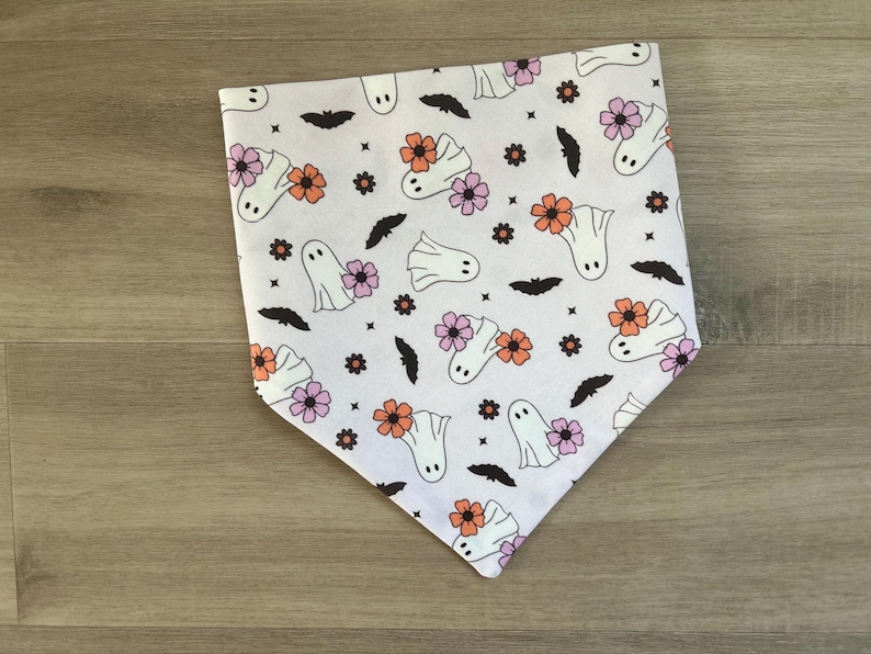 K&ouml;nnte beinhalten: Wei&szlig;es Bandana mit einem sich wiederholenden Muster aus Geistern und Blumen in Rosa, Orange und Wei&szlig;. Das Bandana ist aus Baumwollstoff.