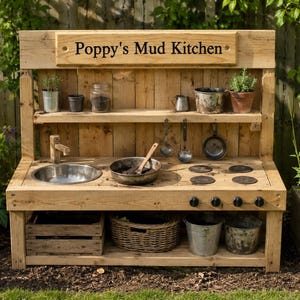 May include: A wooden mud kitchen with the text "Poppy's Mud Kitchen". It has a sink, hob, shelves with pots and plants, and storage below. The kitchen is made of light-coloured wood and is set in a garden setting.