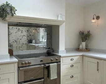Puede incluir: Una cocina blanca con una cocina de acero inoxidable y un salpicadero de espejo desgastado. La cocina cuenta con gabinetes blancos con herrajes de níquel cepillado y una encimera blanca.