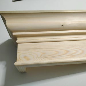 May include: Unfinished wooden shelf with a decorative moulding around the top edge. The shelf is made of light-coloured wood with a natural grain pattern.