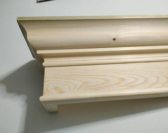 May include: Unfinished wood shelf with a decorative molding around the top edge. The shelf is made of light-colored wood with a natural grain pattern.