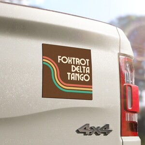 May include: A brown square car magnet with a retro design. The magnet features a wavy, multi-colored stripe pattern and the text "FOXTROT DELTA TANGO".