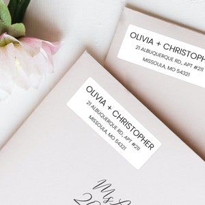 May include: Two white rectangular address labels with black text. The text reads "Olivia + Christopher" followed by the address "21 Albuquerque Rd., Apt #211, Missoula, MO 54321".