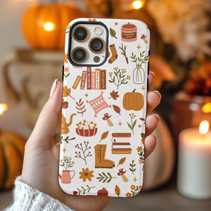 May include: White iPhone case with a fall-themed design. The case features illustrations of pumpkins, leaves, books, a boot, a teapot, and a candle. The text "Pumpkin Spice" is visible on the candle.