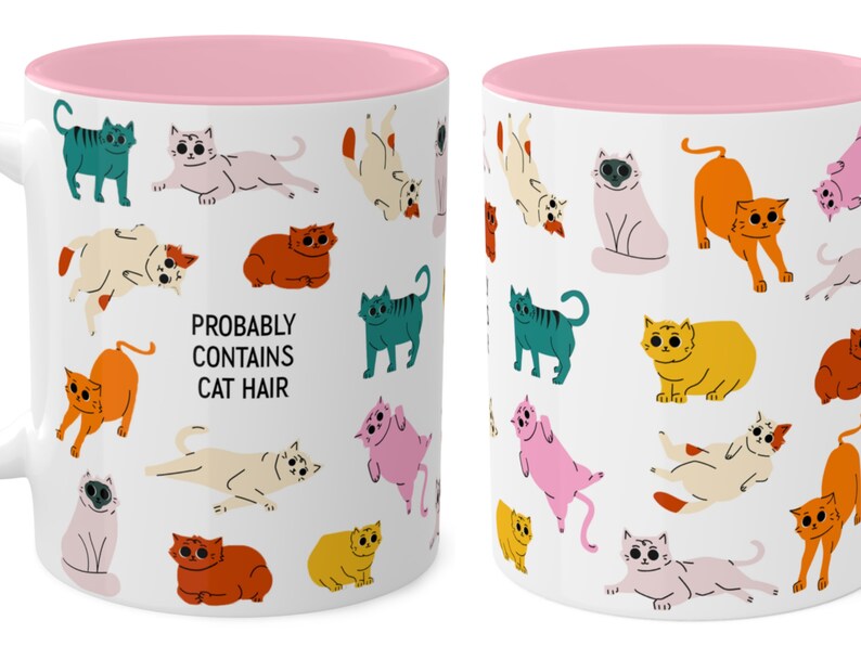 May include: White ceramic mug with a pink rim. The mug features a repeating pattern of colourful cartoon cats in various poses. The text "PROBABLY CONTAINS CAT HAIR" is printed in black on the mug.